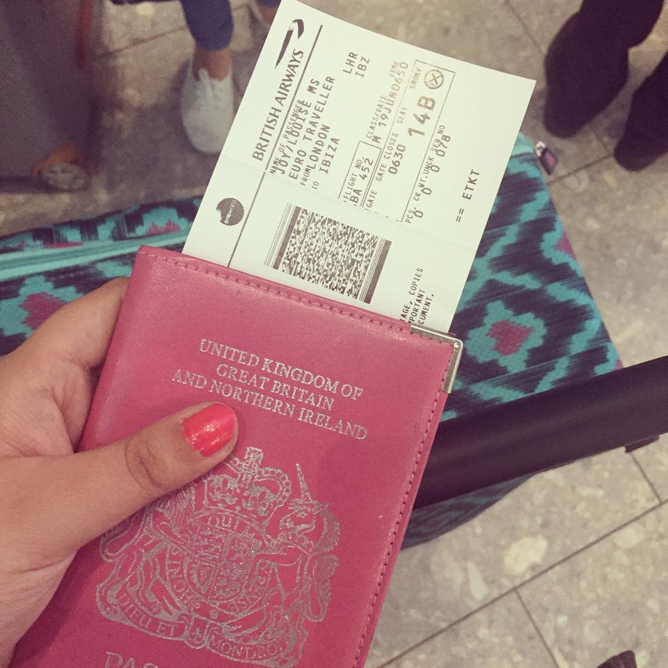 Louise is holding her passport in a pink passport cover, with her plane ticket to Ibiza tucked between the pages. She has bright pink nails and her friend's blue suitcase is in the background of the photo, signalling the start of their holiday!