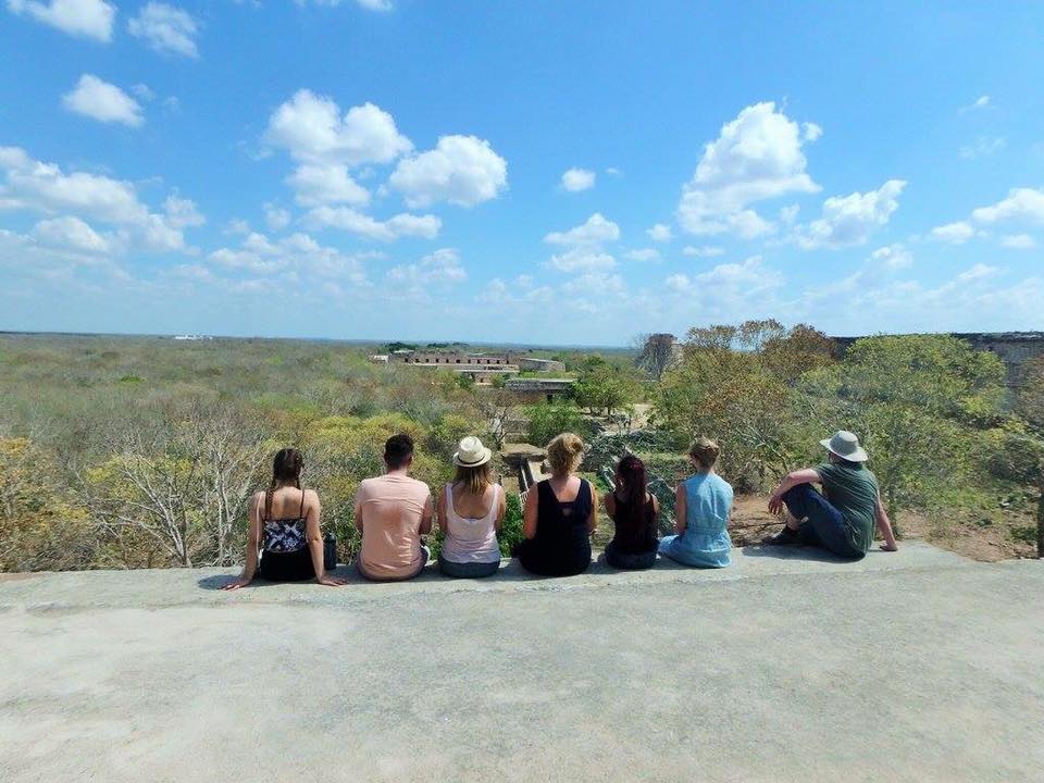 Louise and her tour mates sitting at the very top of one of the pyramids in Uxmal. Beyond them is the bright blue sky and lush green jungle.