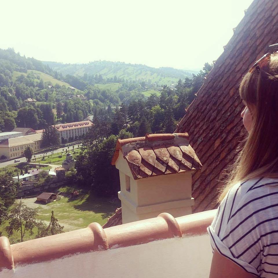Louise overlooking the countryside surrounding Bran Castle, Brasov in Romania. There are mountains in the distance and a turret-like structure in front of her.