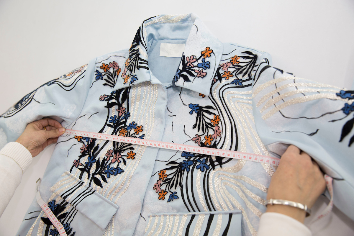 A lady is measuring a pale blue dress from H&M which is covered in pretty floral patterns. H&M is one of the brands dedicated to helping quit fast fashon.