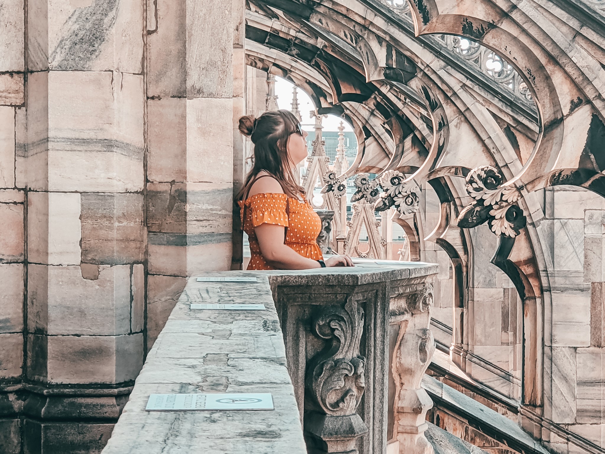 Louise posing at Duomo di Milano in Milan, Italy. She is wearing a mustard yellow dress with white polka dots, and the grey stone of the stunning arches surround her.