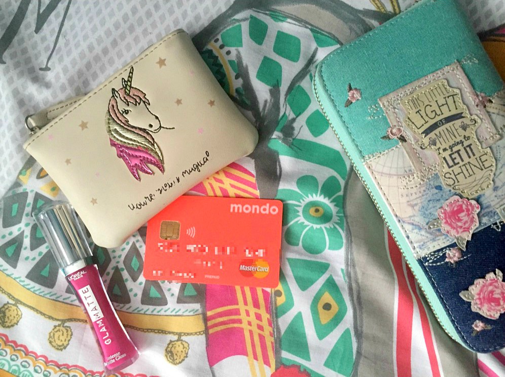 A collection of money-related accessories, from a small white coin purse (with a unicorn stitched on the front) to a large vintage purse which can hold cards and more. There's a bright pink/coral Monzo card spilling put of one of the purses, with the details pixelated so no one can read it.