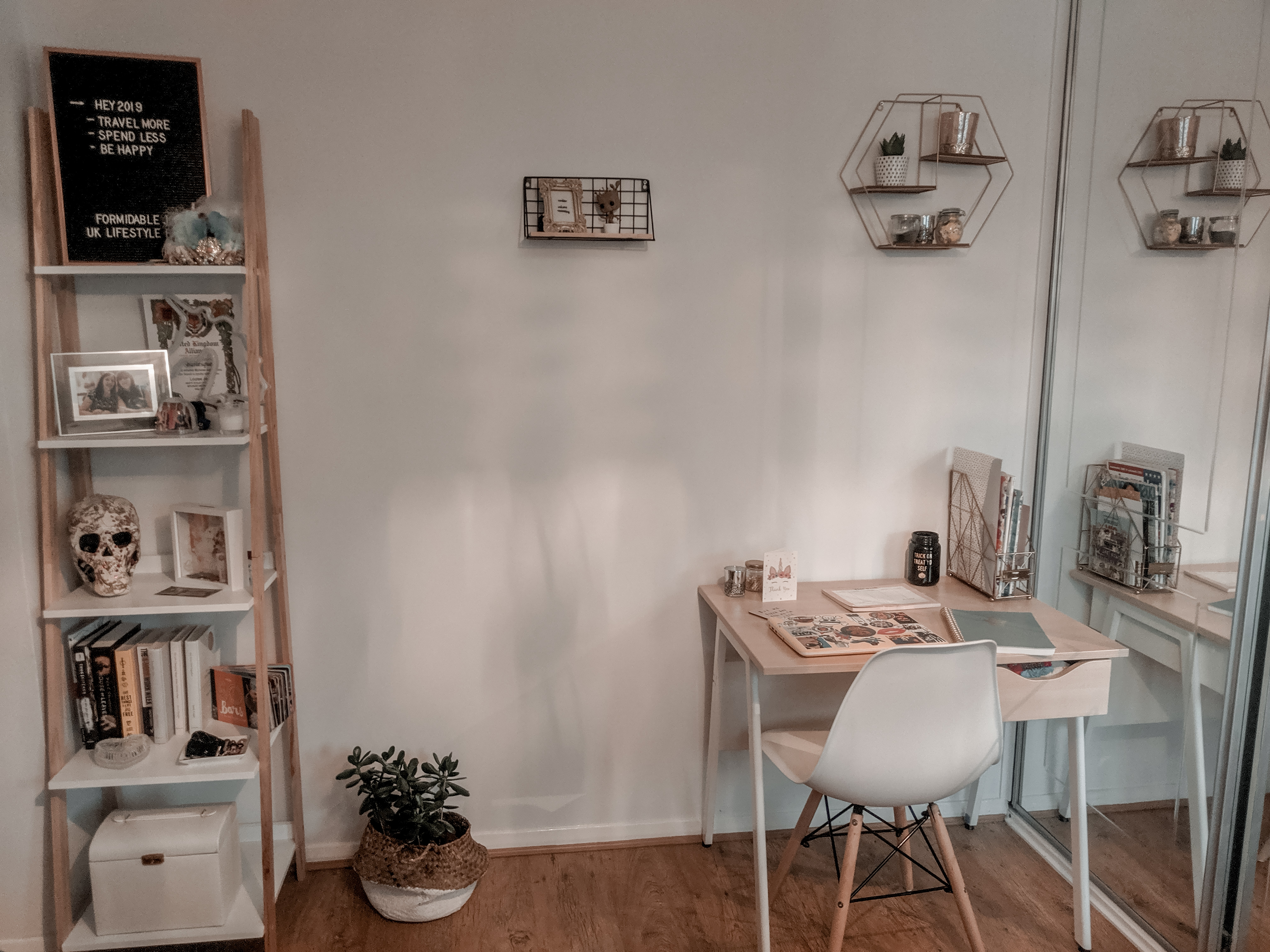 Inside Louise's room, with bright white walls and pine accessories. There is a small pine desk to the right and on the left is a ladder shelf, filled with books and photographs.