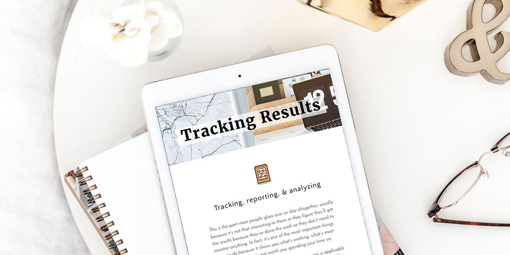 A neatly arranged desk features a tablet displaying a document titled "Tracking Results." Next to the tablet is a spiral notebook with a pen. Decor items include a gold ampersand symbol, a small potted plant, and white flowers in a vase, alongside notes on 3 free online courses to take during quarantine, creating an organized workspace.